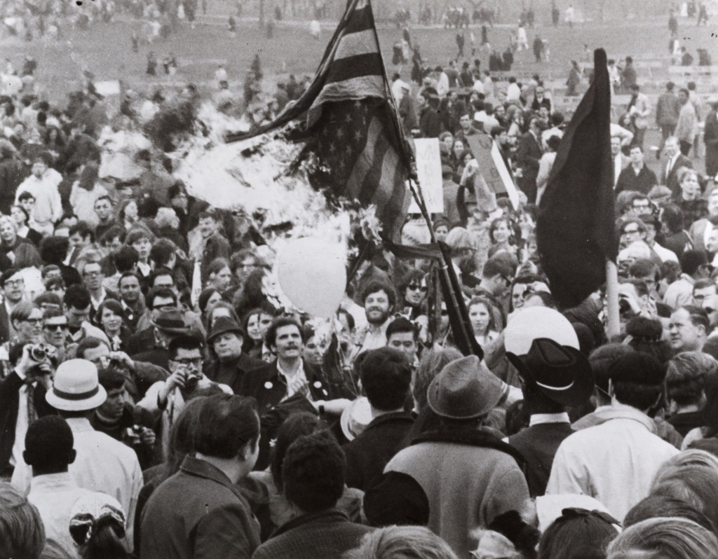Black and white photo shows protesters burning an American flag in Central Park.