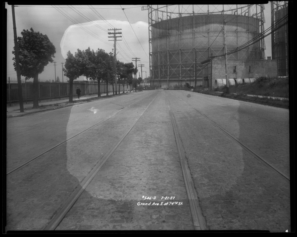 Black and white photograph displaying large gas tanks in the distance.