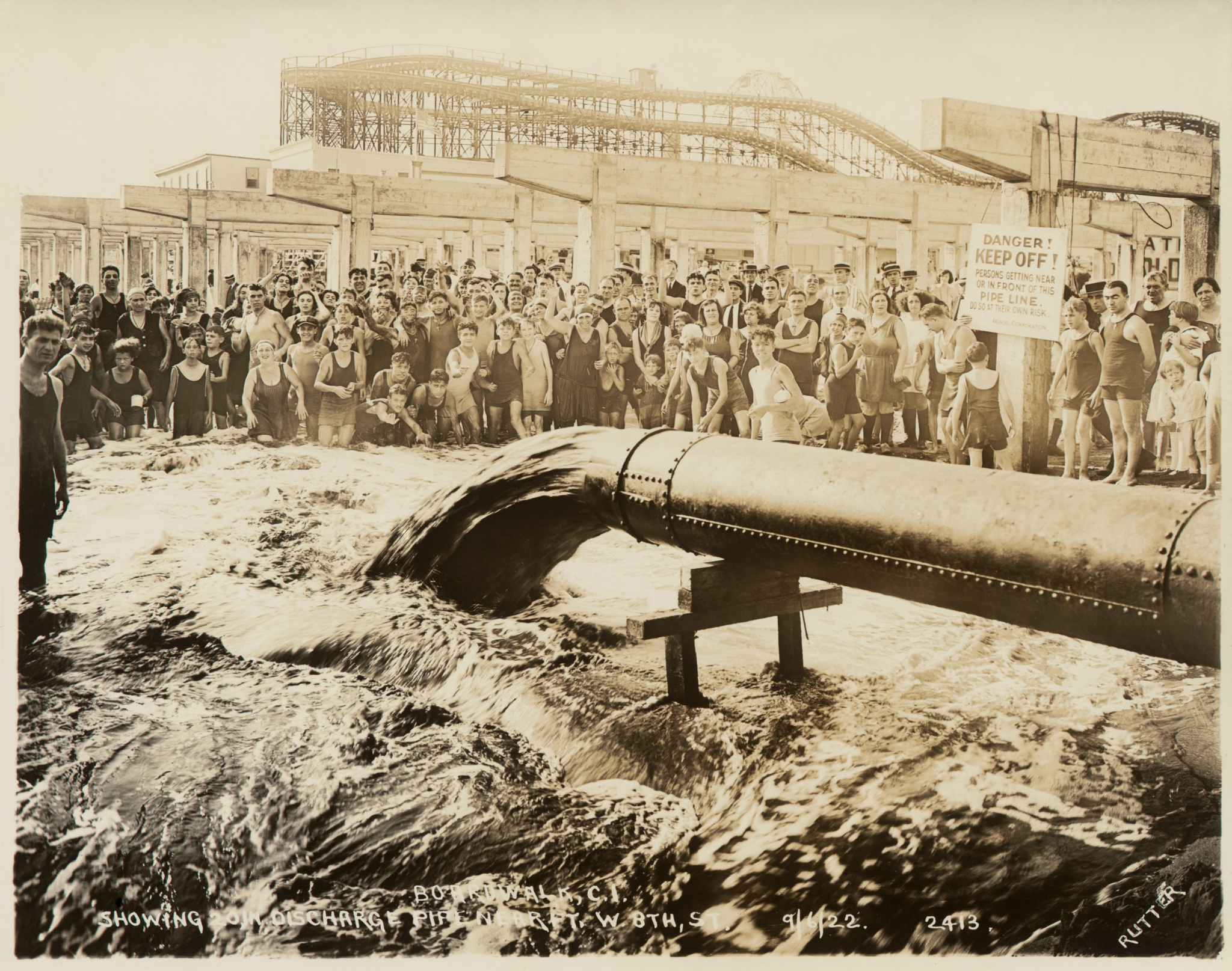 Photograph showing bathers and onlookers observing discharge pipe onto beach near west 8th.